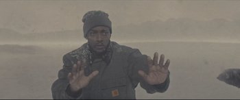 Movie still from “Synchronic” (2019), directed by Justin Benson – A man in a winter coat and a hat is holding his hands up in front of him; Medium shot, Low angle