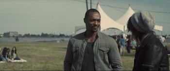 Movie still from “Synchronic” (2019), directed by Justin Benson – A man standing in front of a white tent in a field; Medium shot, Over the shoulder angle