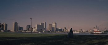 Movie still from “Synchronic” (2019), directed by Justin Benson – A man sitting on a grassy hill in front of a city skyline; Extreme Wide shot, Over the shoulder angle