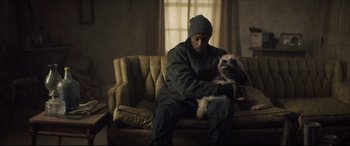 Movie still from “Synchronic” (2019), directed by Justin Benson – A man sitting on top of a couch holding a dog; Medium shot, High angle