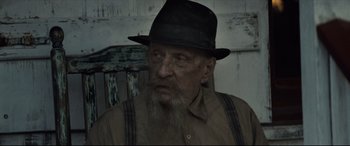 Movie still from “Synchronic” (2019), directed by Justin Benson – An old man with a beard wearing a black hat; Close Up shot, Low angle