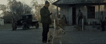 Movie still from “Synchronic” (2019), directed by Justin Benson – A man and a dog are standing in front of a barn; Medium shot, Low angle