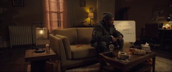 Movie still from “Synchronic” (2019), directed by Justin Benson – A man sitting on a couch in front of a coffee table; Wide shot, Over the shoulder angle