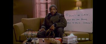 Movie still from “Synchronic” (2019), directed by Justin Benson – A man sitting on a couch holding a pair of shoes; Medium shot, High angle