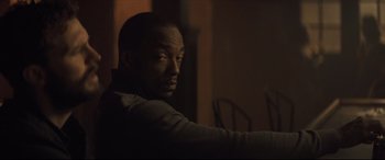 Movie still from “Synchronic” (2019), directed by Justin Benson – A man sitting in a dark room looking at the camera; Close Up shot, Over the shoulder angle
