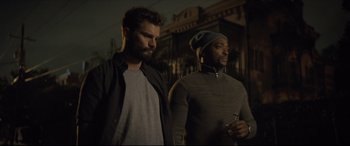 Movie still from “Synchronic” (2019), directed by Justin Benson – A couple of men standing next to each other on a street; Medium shot, Over the shoulder angle
