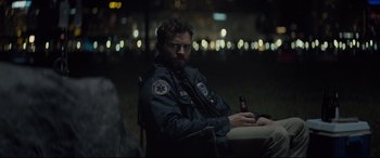 Movie still from “Synchronic” (2019), directed by Justin Benson – A man sitting in a chair holding a bottle of beer; Medium shot, Over the shoulder angle