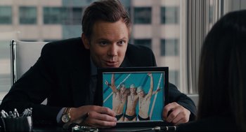 Movie still from “Ted” (2012), directed by Seth MacFarlane – A man in a suit holding a picture of two men in swim trunks; Medium shot, Over the shoulder angle