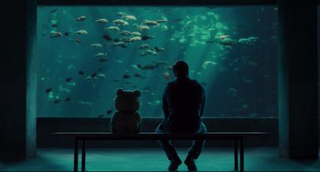 Movie still from “Ted” (2012), directed by Seth MacFarlane – A person sitting on top of a bench looking at an aquarium; Wide shot, Over the shoulder angle