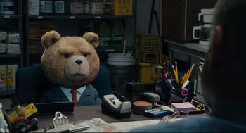 Movie still from “Ted” (2012), directed by Seth MacFarlane – A teddy bear sitting at a desk in front of a chair; Medium shot, Over the shoulder angle