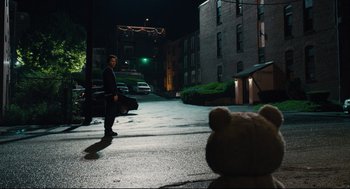 Movie still from “Ted” (2012), directed by Seth MacFarlane – A man standing on the side of the road next to a teddy bear; Wide shot, Over the shoulder angle