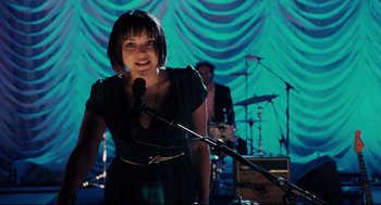 Movie still from “Ted” (2012), directed by Seth MacFarlane – A woman standing in front of a microphone on a stage; Medium shot, Over the shoulder angle