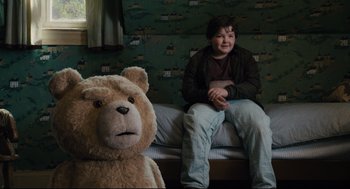 Movie still from “Ted” (2012), directed by Seth MacFarlane – A boy sitting on a bed next to a large teddy bear; Medium shot, Overhead angle