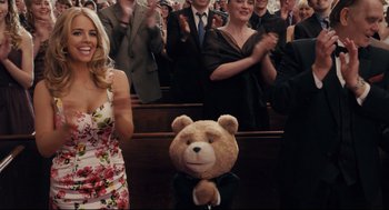 Movie still from “Ted” (2012), directed by Seth MacFarlane – A crowd of people sitting in a room with a teddy bear; Medium shot, Low angle