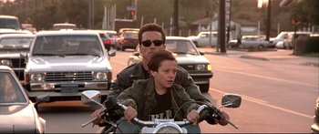 Movie still from “Terminator 2: Judgment Day” (1991), directed by James Cameron – A man and a boy riding a motorcycle down a street; Medium shot, Low angle