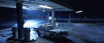 Movie still from “Terminator 2: Judgment Day” (1991), directed by James Cameron – A police car parked at a gas station at night; Wide shot, High angle