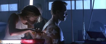 Movie still from “Terminator 2: Judgment Day” (1991), directed by James Cameron – A man is getting his chest cut off by a woman; Medium shot, Low angle