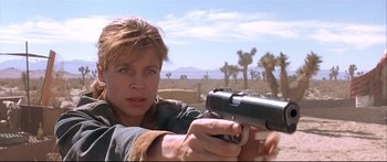 Movie still from “Terminator 2: Judgment Day” (1991), directed by James Cameron – A woman holding a gun while standing in a field; Close Up shot, Low angle