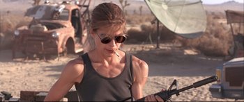 Movie still from “Terminator 2: Judgment Day” (1991), directed by James Cameron – A woman smoking a cigarette while looking at a cell phone; Medium shot, Low angle