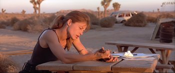 Movie still from “Terminator 2: Judgment Day” (1991), directed by James Cameron – A woman writing on a piece of paper on top of a table; Close Up shot, Low angle