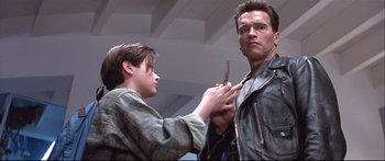 Movie still from “Terminator 2: Judgment Day” (1991), directed by James Cameron – A man is cutting another man's hair with a pair of shears; Close Up shot, Low angle