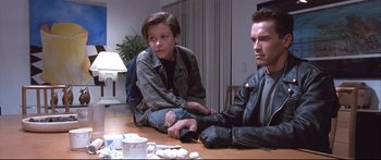 Movie still from “Terminator 2: Judgment Day” (1991), directed by James Cameron – A man and a boy sitting at a table; Medium shot, Low angle