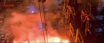 Movie still from “Terminator 2: Judgment Day” (1991), directed by James Cameron – A person standing on a platform in front of a fire; Wide shot, Overhead angle