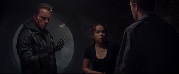 Movie still from “Terminator Genisys” (2015), directed by Alan Taylor – A woman standing in a dark room next to a mirror; Medium shot, Over the shoulder angle