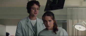 Movie still from “Terminator Genisys” (2015), directed by Alan Taylor – A young man standing next to a young woman in front of a television; Medium shot, Over the shoulder angle