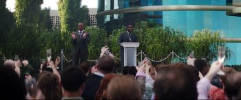 Movie still from “Terminator Genisys” (2015), directed by Alan Taylor – Two men in business suits giving a speech to an audience; Wide shot, Over the shoulder angle