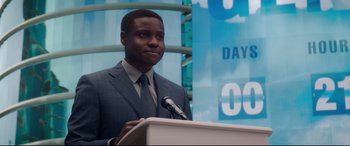 Movie still from “Terminator Genisys” (2015), directed by Alan Taylor – A man standing at a podium with a microphone; Medium shot, Over the shoulder angle