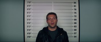 Movie still from “Terminator Genisys” (2015), directed by Alan Taylor – A man standing in front of a wall with his mugshot on it; Medium shot, Overhead angle