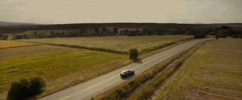 Movie still from “Texas Chainsaw Massacre” (2022), directed by David Blue Garcia – A car driving down a road near a grassy field; Extreme Wide shot, High angle