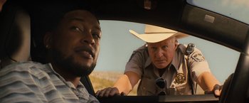 Movie still from “Texas Chainsaw Massacre” (2022), directed by David Blue Garcia – A man in a hat is looking out the window of a car while another man in a hat looks on; Close Up shot, Over the shoulder angle