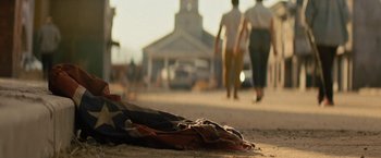 Movie still from “Texas Chainsaw Massacre” (2022), directed by David Blue Garcia – An american flag laying on the ground in the middle of the street; Wide shot, Low angle