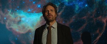 Movie still from “The Adam Project” (2022), directed by Shawn Levy – A man in a suit and tie standing in front of a space background; Medium shot, Low angle