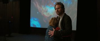 Movie still from “The Adam Project” (2022), directed by Shawn Levy – A man and a child hug in front of a projector screen; Medium shot, Over the shoulder angle