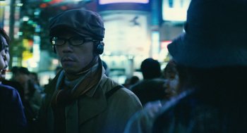 Movie still from “Babel” (2006), directed by Alejandro G. Iñárritu – A man wearing a hat and glasses while standing in a crowd of people; Close Up shot, Low angle
