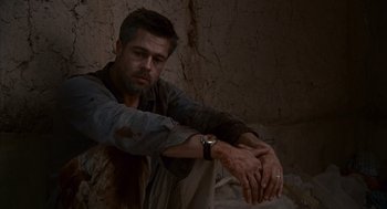 Movie still from “Babel” (2006), directed by Alejandro G. Iñárritu – A man sitting on the ground with his hands on his knees; Medium shot, Low angle