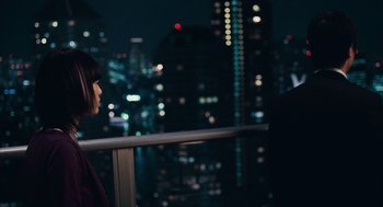 Movie still from “Babel” (2006), directed by Alejandro G. Iñárritu – A man and a woman standing next to a railing in front of a city skyline at night; Medium shot, Over the shoulder angle