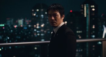 Movie still from “Babel” (2006), directed by Alejandro G. Iñárritu – A man standing in front of a city skyline at night; Close Up shot, Low angle