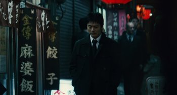 Movie still from “Babel” (2006), directed by Alejandro G. Iñárritu – A man wearing a suit and tie standing in front of a building; Medium shot, Low angle