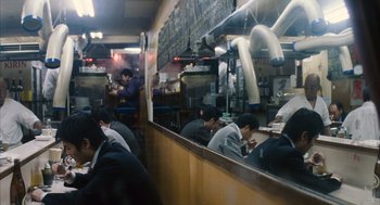 Movie still from “Babel” (2006), directed by Alejandro G. Iñárritu – A group of people sitting at a table in front of a counter; Wide shot, High angle