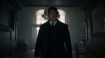 Movie still from “The Alienist” (2018), created by Cary Joji Fukunaga – A man wearing a suit and tie in a dark room; Medium shot, Low angle