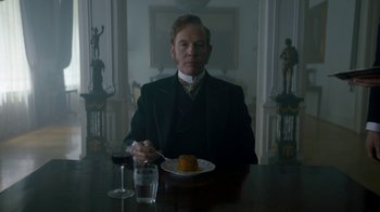 Movie still from “The Alienist” (2018), created by Cary Joji Fukunaga – A man sitting at a table with a glass of wine; Medium shot, Low angle