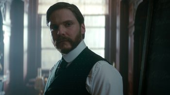 Movie still from “The Alienist” (2018), created by Cary Joji Fukunaga – A man with a goatee wearing a white shirt and a vest; Close Up shot, Low angle