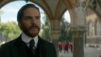 Movie still from “The Alienist” (2018), created by Cary Joji Fukunaga – A man with a beard wearing a suit and tie in front of a crowd; Close Up shot, Over the shoulder angle