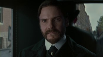 Movie still from “The Alienist” (2018), created by Cary Joji Fukunaga – A person wearing a suit and tie; Close Up shot, Low angle