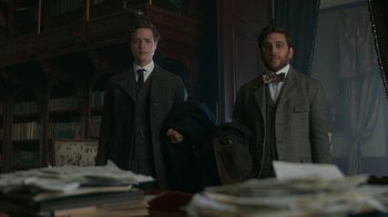 Movie still from “The Alienist” (2018), created by Cary Joji Fukunaga – Two men in suits and bow ties standing in front of a pile of papers; Medium shot, Low angle