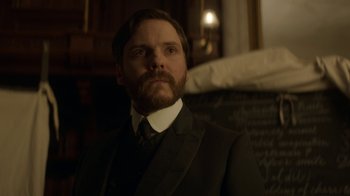Movie still from “The Alienist” (2018), created by Cary Joji Fukunaga – A man in a suit and tie standing in front of a bed; Close Up shot, Low angle
